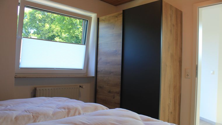 A bright bedroom with two beds and a large window. A modern wardrobe is against the wall, and the atmosphere is friendly and inviting.