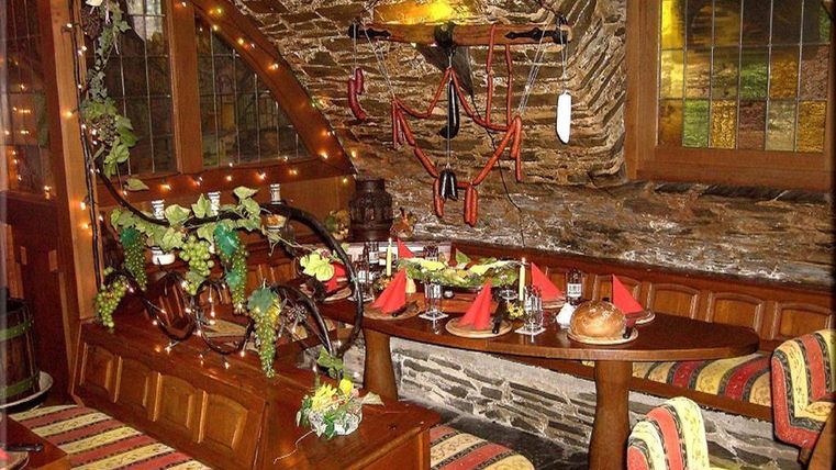 Eine gemütliche Restaurant-Ecke mit Holzverkleidung und bunten Kissen. Der Tisch ist festlich gedeckt und mit Pflanzen dekoriert.