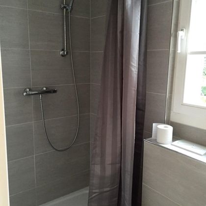 A modern shower in a bright bathroom. The walls are lined with gray tiles and a shower curtain provides privacy.