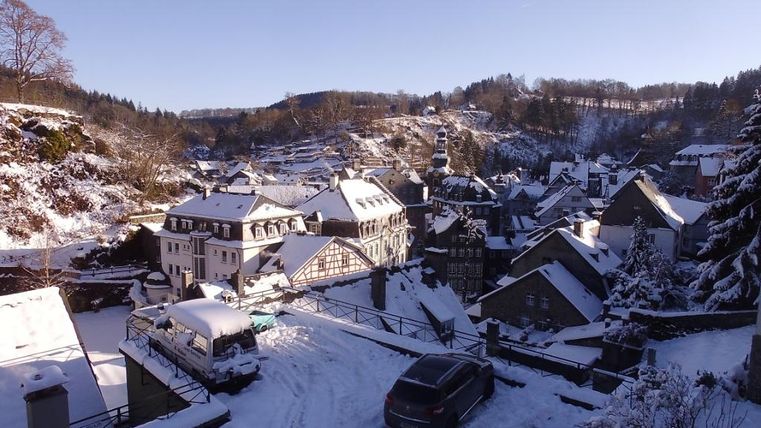 A snowy cityscape with traditional houses and snowy rooftops. The sky is clear and bright blue.