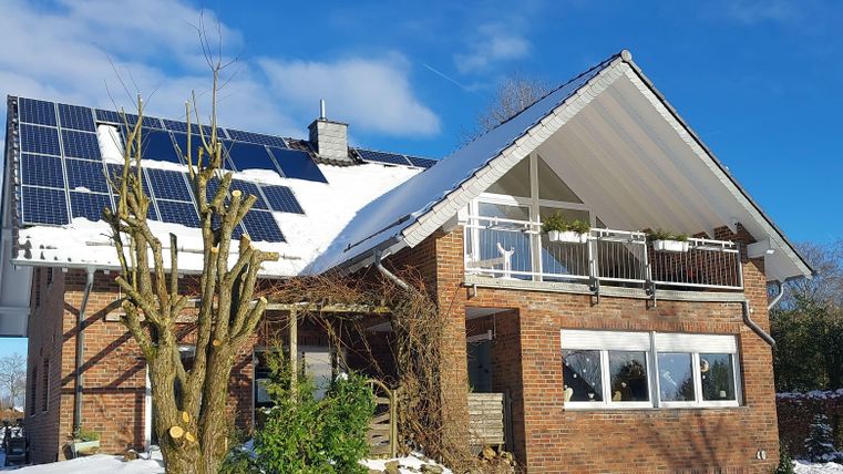 A modern house with solar panels on the roof. It is located in a snowy environment under a clear blue sky.