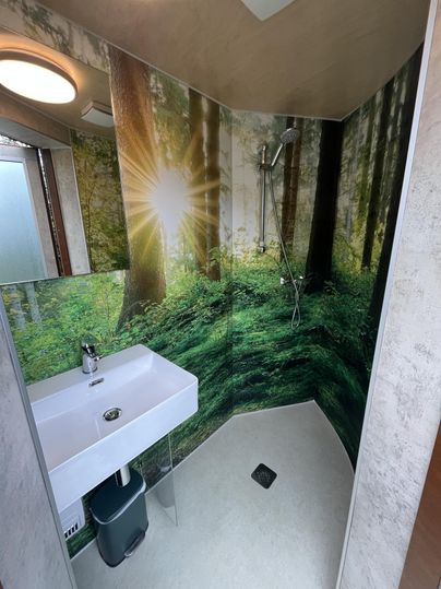Een moderne douche met een wastafel en een bosafbeelding aan de muur. Het licht straalt door de bomen en creëert een rustgevende sfeer.
