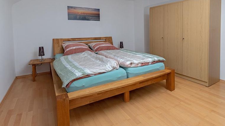 Ein gemütliches Schlafzimmer mit einem großen Doppelbett und Holzmöbeln. Die Wände sind neutral und der Boden ist aus hellem Holz, was eine einladende Atmosphäre schafft.