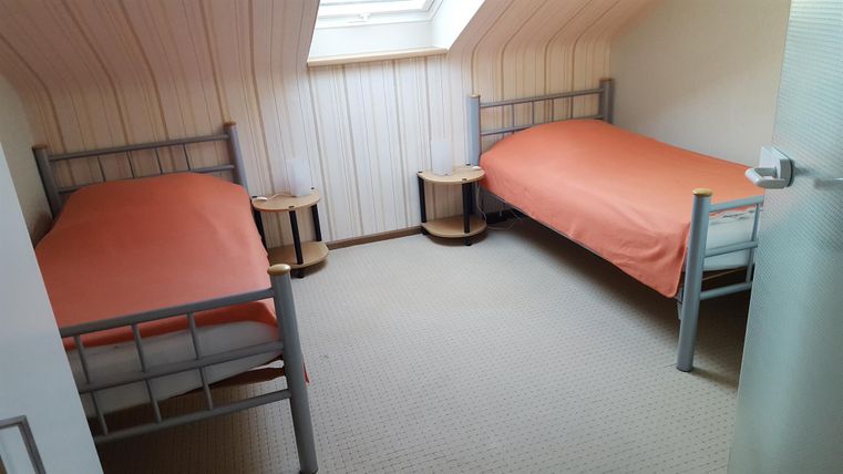Een gezellige kamer met twee eenpersoonsbedden en oranje beddengoed. De kamer heeft een dakraam en een lichte tapijtvloer.