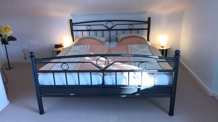 Een gezellig slaapkamer met een tweepersoonsbed en zachte verlichting. Aan de wand staat een bloem in een vaas, die de ruimte een uitnodigende sfeer geeft.