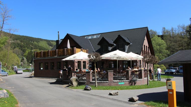 A charming restaurant with a terrace and sun umbrellas. It is located in a quiet setting, surrounded by trees.