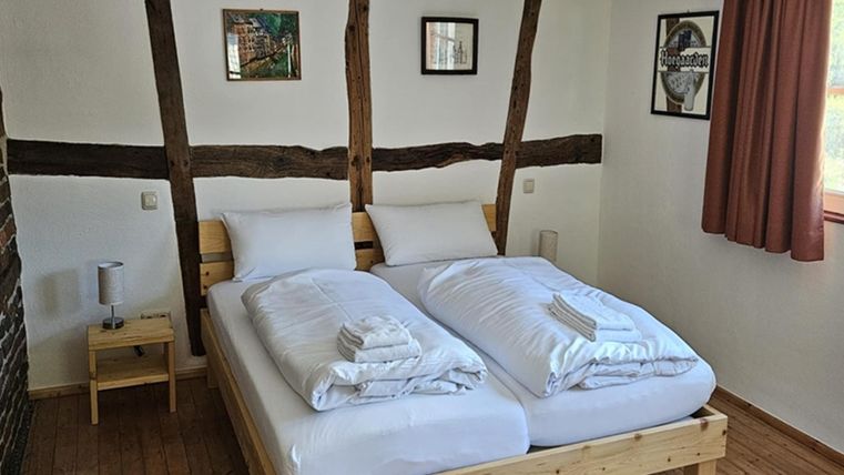 A cozy bedroom with a double bed and bright bedding. The walls are decorated with wooden strips and there are some pictures as well as a window with a curtain.