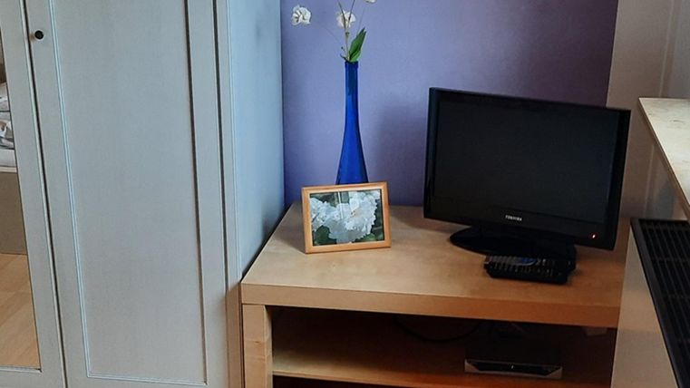A cozy room with a television on a wooden cabinet. On the table sits a vase with flowers and a framed picture.