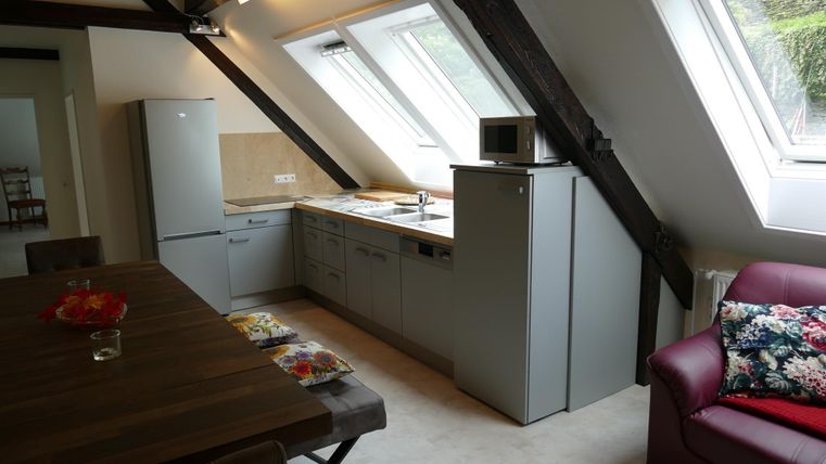 Een moderne keuken met groene kasten en lichte muren. Op de voorgrond staat een stijlvolle eettafel en een gezellige bank.