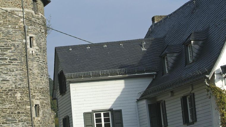 Een historisch gebouw met een stenen toren en een wit huis. Het dak van het huis heeft mooie details en de ramen zijn voorzien van groene luiken.