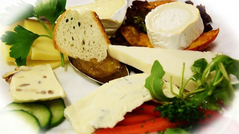 Een bord met verschillende kaassoorten, verse groenten en brood. Daarbovenop is er een zoete fruitsalade.