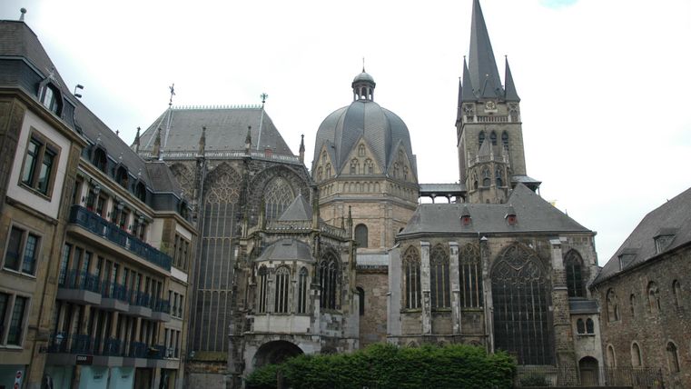 An impressive church with distinctive towers and Gothic architecture. The buildings surround a small square with some modern residential houses.