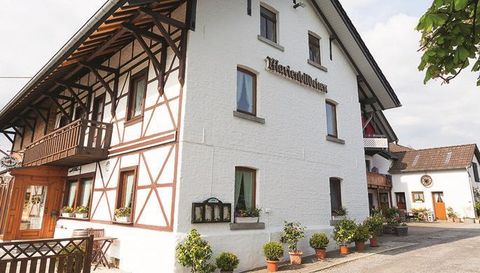 A charming half-timbered house with an inviting entrance. The facade is white with wood-accented elements and decorative plants.
