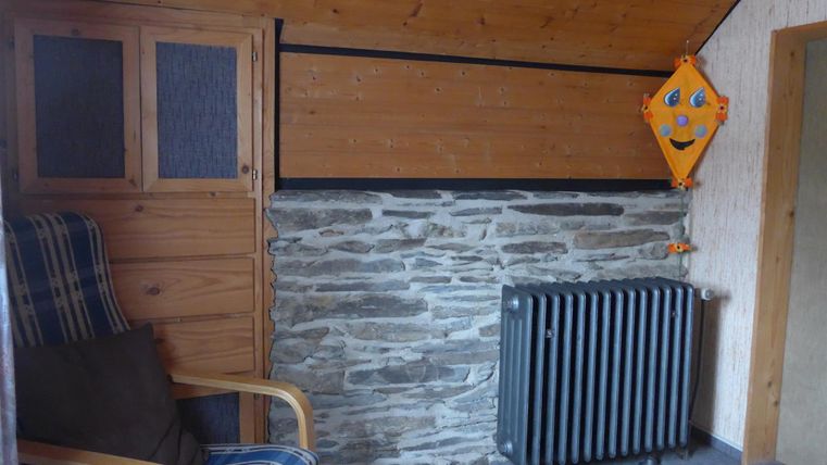 A cozy room with an armchair and a radiator. The walls are made of wood and stone, and a child figurine is mounted on the wall.