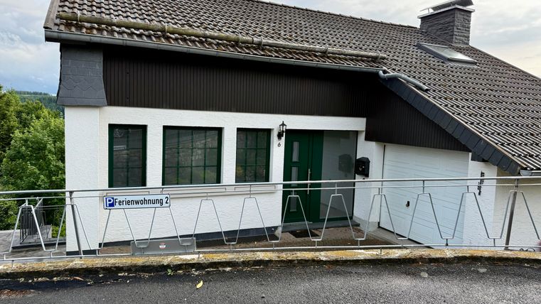 Een modern vakantiehuis met witte muren en een schuin dak. De façade toont grote ramen en een bord met de tekst "Vakantiehuis 2".