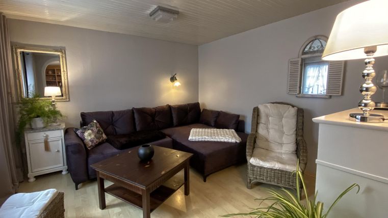 A cozy living room with a dark brown sofa and a table. A floor lamp and plants create an inviting atmosphere.
