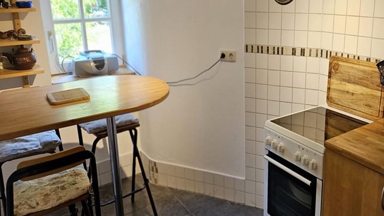 A small, modern kitchen with a dining table and chairs. The room has white tiled walls and a cooking area.