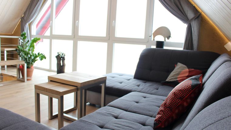 A cozy living room with a gray sofa and two small tables. Large windows let in plenty of light, creating an inviting atmosphere.