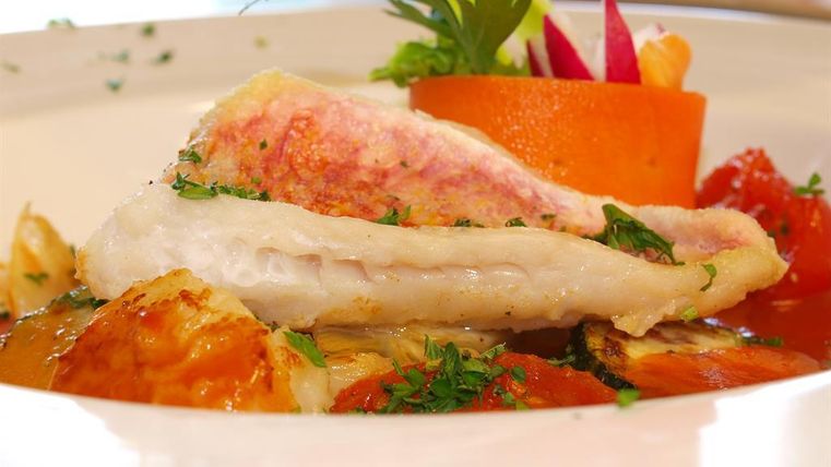 Ein perfekt zubereiteter Fischfilet, garniert mit frischen Kräutern. Daneben befinden sich bunte Gemüsedekorationen und eine ansprechende Präsentation auf dem Teller.