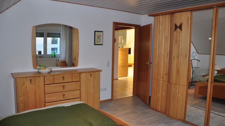 A cozy bedroom with wooden flooring and modern furniture. The room includes a mirror and a large wardrobe.