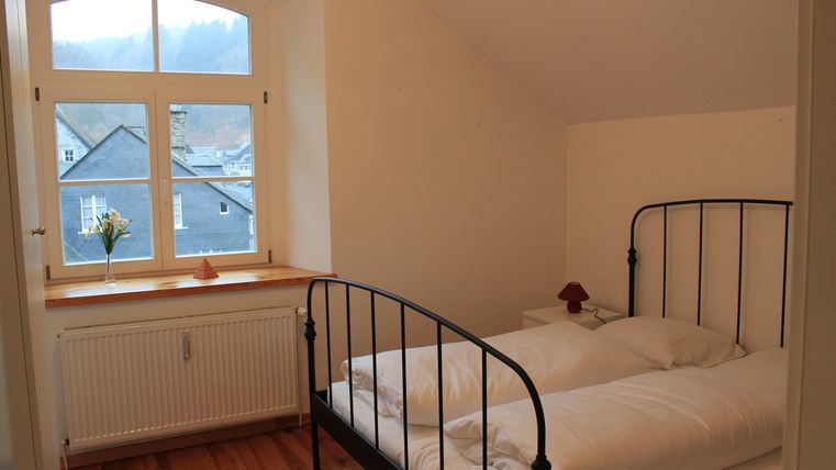 Een eenvoudige slaapkamer met een metalen bed en vers opgemaakte dekbedden. Het raam biedt uitzicht op een rustige landschap en een klein boeketje staat op de vensterbank.