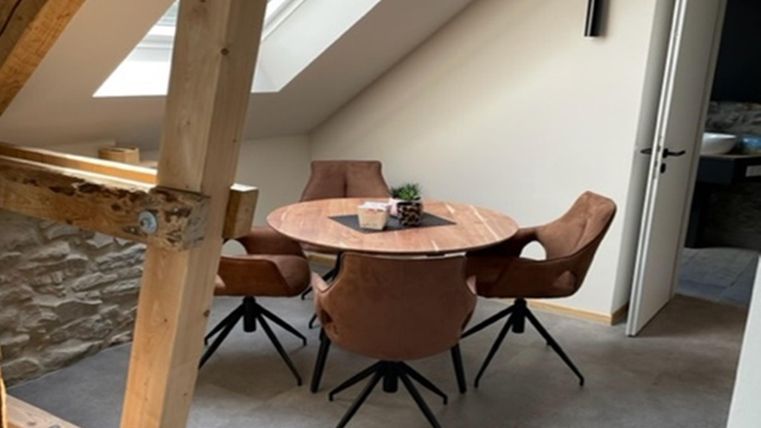 Een gezellige eetruimte met een ronde houten tafel en vier stoelen. Grote ramen zorgen voor veel daglicht en een aangename sfeer.
