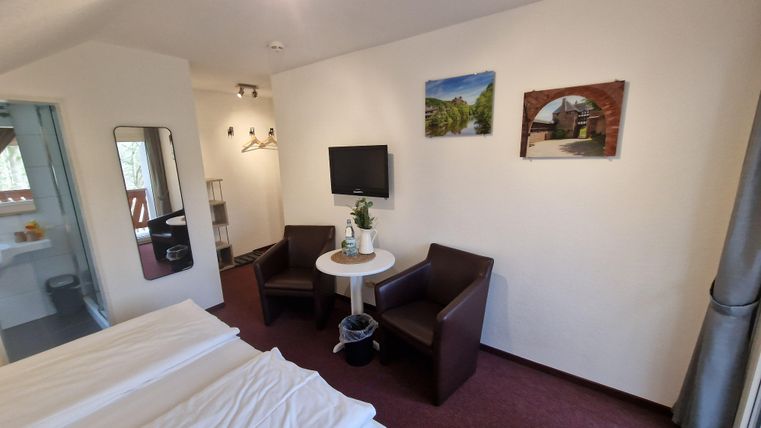 A cozy room with two beds, a table, and two chairs. Pictures hang on the wall, and there is a television.