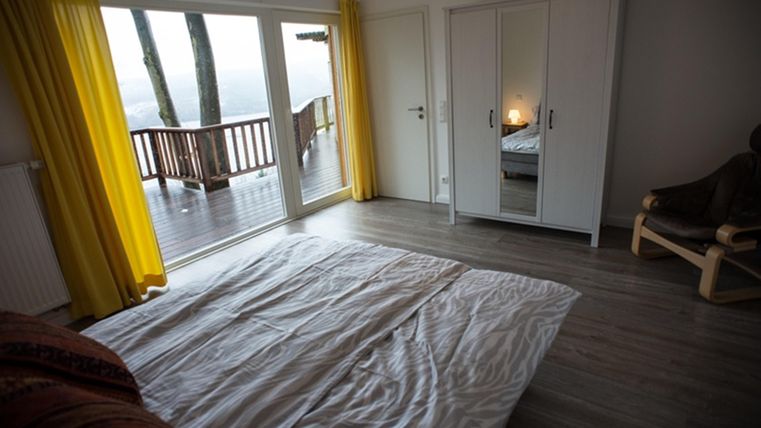 A bright room with a bed and large windows overlooking a terrace. Yellow curtains give the room a cheerful atmosphere.