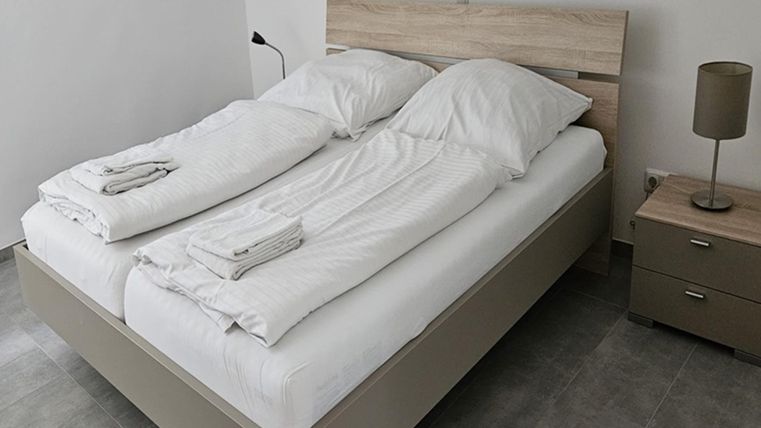 Een moderne slaapkamer met een tweepersoonsbed en frisse beddengoed. Naast het bed staat een nachtkastje met een lamp.