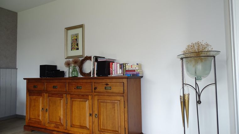 Een elegant houten sideboard staat tegen een muur. Naast staat een decoratieve plant in een glazen vaas.