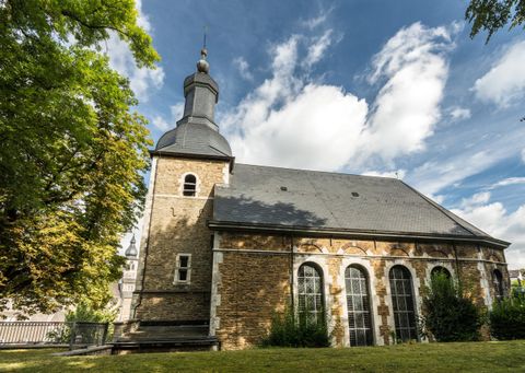 Eine charmante Kirche mit einem schwarzen Dach und einem charakteristischen Turm. Umgeben von Bäumen und einem klaren Himmel.