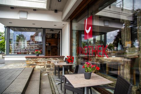 An inviting café with a large window front and blooming plants in front of the door. The modern architecture and cozy atmosphere invite you to linger.