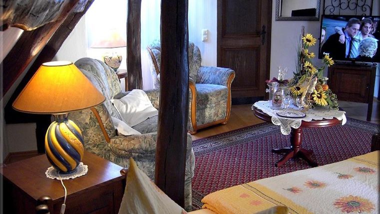 Ein gemütlicher Wohnbereich mit stilvollen Möbeln, einem dekorativen Tisch und einer Lampe. Im Hintergrund ist ein Fernseher sichtbar.
