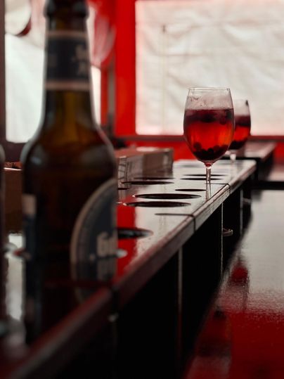 Een tafel met een bier en een glas rode drank. Op de achtergrond zijn meer glazen zichtbaar.