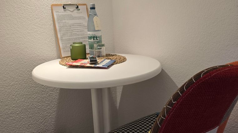 A small table with a colorful chair, a bottle of water, and a notepad. Next to the table stands a trash can.