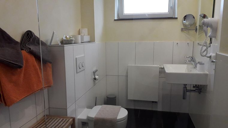 Ein modernes Badezimmer mit weißen Fliesen und einem kleinen Waschbecken. Handtücher und Pflegeartikel sind ordentlich angeordnet.