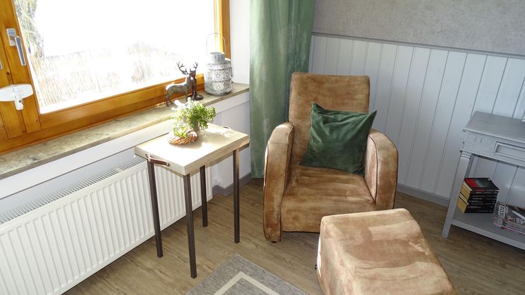 Een gezellige ruimte met een comfortabele fauteuil en een kleine tafel. Bij een raam met natuurlijk licht staan planten en een decoratieve lamp.