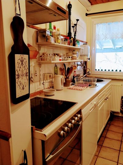 Een gezellige keuken met witte kasten en een fornuis. Op de planken staan verschillende kookgerei en specerijen.