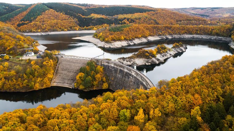 An impressive landscape with a reservoir and colorful forests in autumn. The dam stretches over the calm water.