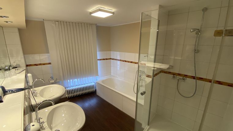 A modern bathroom with a shower and bathtub. It features bright colors and two sinks.