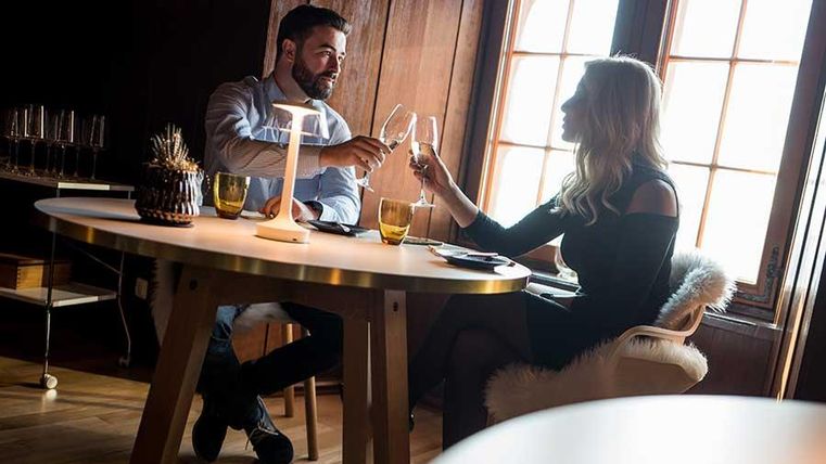 A romantic candlelight dinner. A couple toasts in a cozy room with wooden decor.
