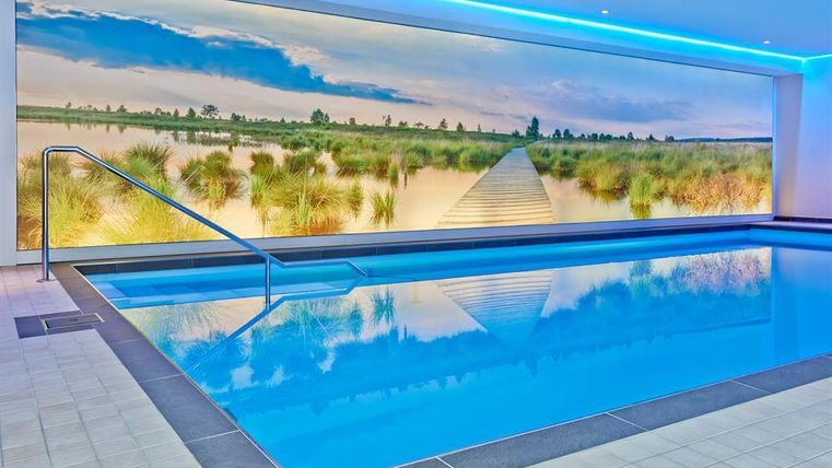 Ein modernes Schwimmbad mit klarem Wasser und einer schönen Wandgestaltung. Der Raum ist in sanften Farben mit LED-Beleuchtung gehalten.