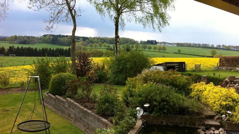 Ein schöner Garten mit viel Grün und bunten Blumen. Im Hintergrund sind Felder und Bäume zu sehen.