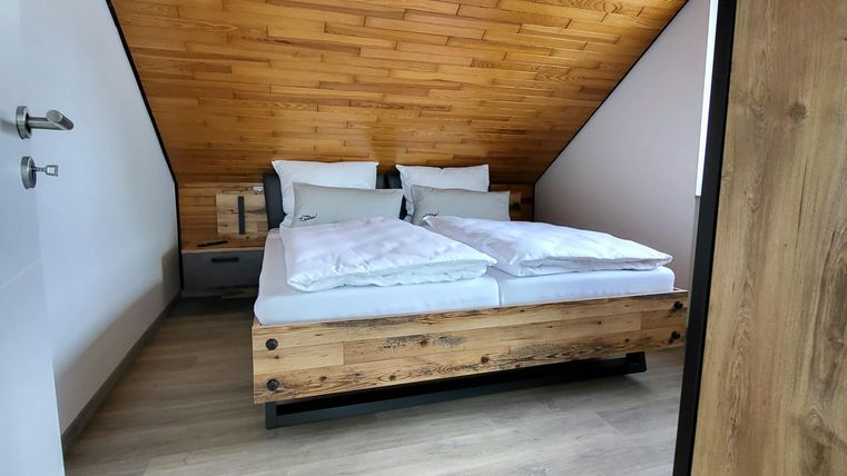 A cozy bedroom with a sloping ceiling. It features a wooden double bed and a warm wooden floor.