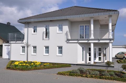 Ein modernes, zweigeschossiges Haus mit einem grauen Dach und großen Fenstern. Der Vorgarten ist mit gelben Blumen und einem schmalen Weg gestaltet.