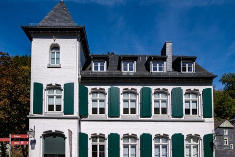 Een historisch gebouw met witte muren en groene shutters. De lucht is helder en blauw.