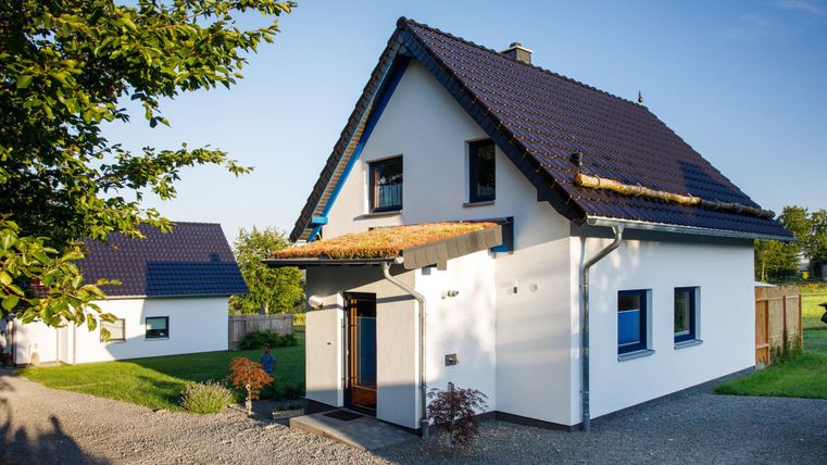 A modern single-family house with a gabled roof and blue window frames. The garden is well-maintained, and the surroundings are green and inviting.