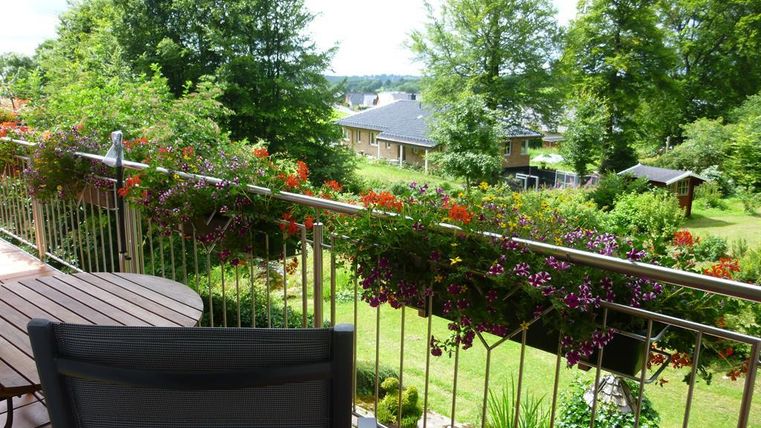 A beautiful balcony with blooming plants and a view of greenery. In the background, single-family houses and trees are visible.