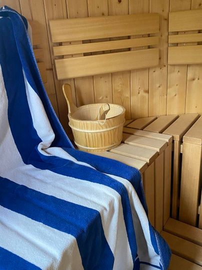 Een gezellige sauna met een houten bank en een selectie handgeweven handdoeken. In de ruimte staat een houten emmer, die op de bank is geplaatst.