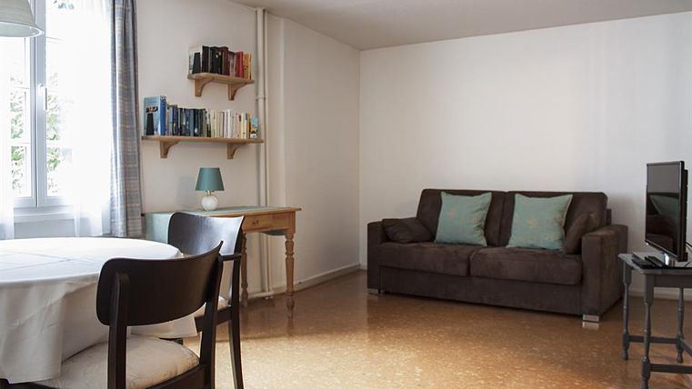 Een moderne woonkamer met een gezellige bank en een tafel. Boekenplanken en een televisie completeren de inrichting.